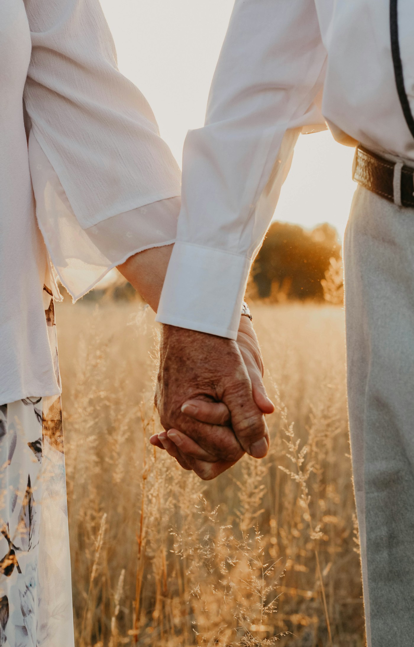 Two people holding hands walking through a field