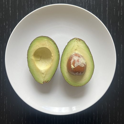 A ripe avocado halved on a white plate